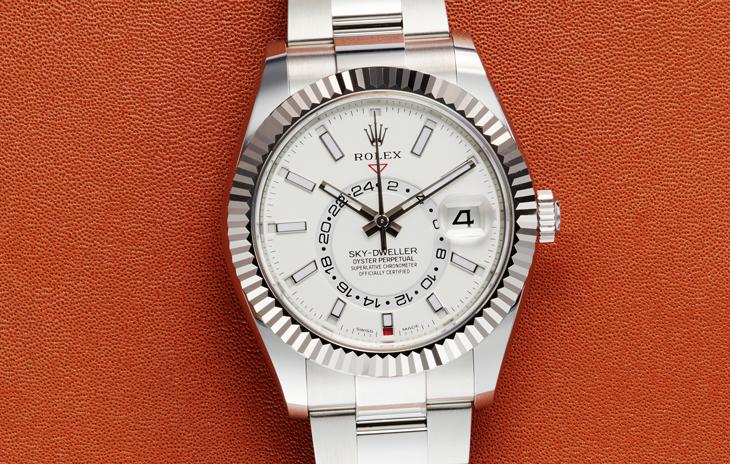 Rolex Sky-Dweller with white dial, fluted bezel, and oyster bracelet on an orange leather background